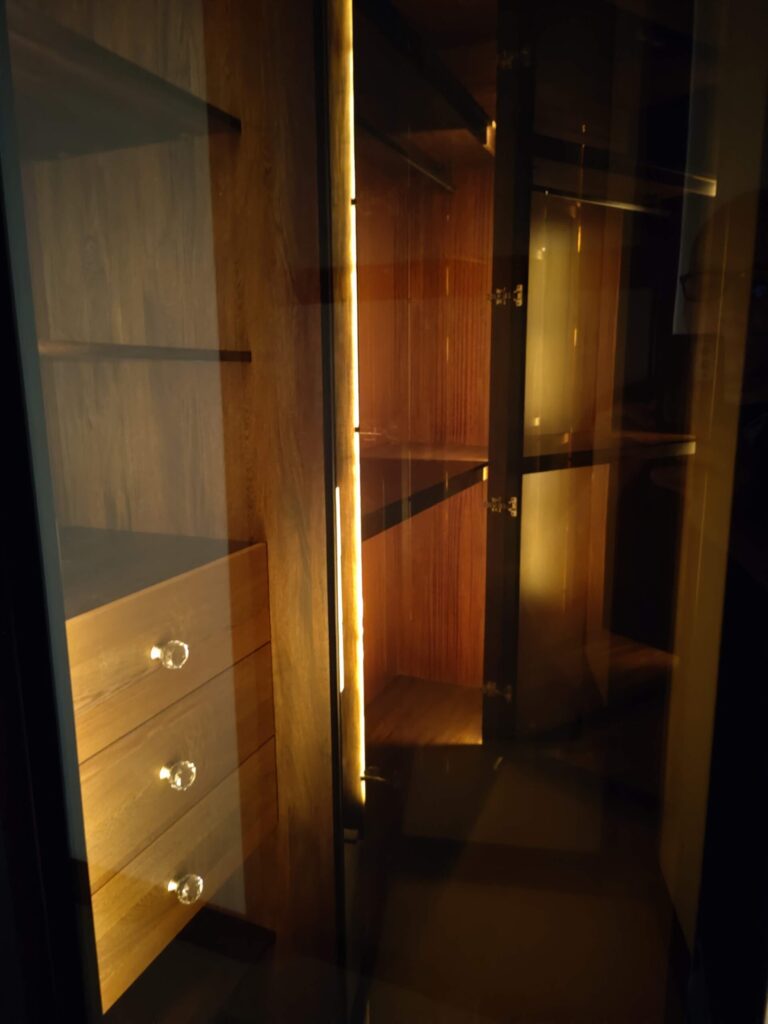 Interior de closet en nogal con iluminación LED cálida en los entrepaños y gavetas de vidrio con tiradores de cristal, Alterra Craft, Tucson, AZ